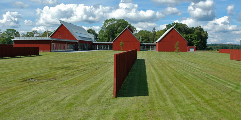 Blick auf drei moderne, rote Holzhäuser auf einem frisch gemähten Rasen