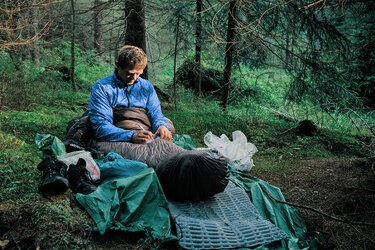 Der Waldwanderer Gerald Klamer sitzt in seinem Schlafsack im Wald und macht sich notizen.