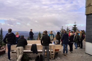 Studierende stehen an einer Berghütte und hören dem Referenten zu