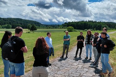 Studierende stehen am Hochwasserrückhaltebecken hören dem Referenten Prof. Bold zu