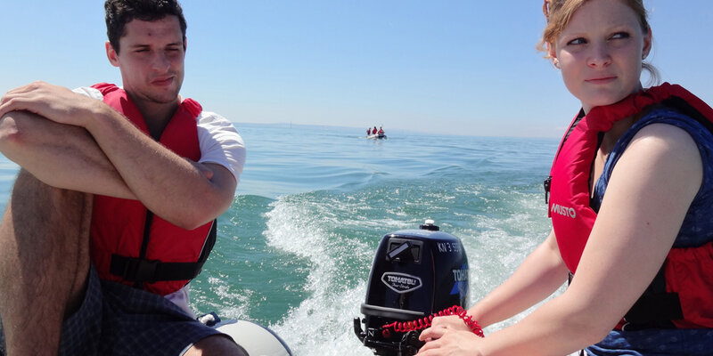 Eine Studentin steuert im Rahmen einer Lehrfahrt ein Motorschlauchboot der Hochschule Rottenburg. Ein Kommilitone sitzt nebenan und genießt das Sommerwetter auf dem Bodensee. 