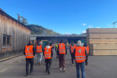 Studierende mit orangenen Warnwesten laufen über das Sägewerksgelände