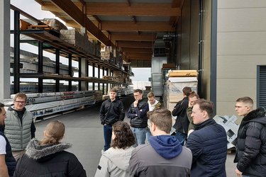 Studierende stehen auf dem Firmengelände und hören dem Referenten zu