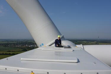 Student sitz auf der Gondel des Windrads und schaut in die Landschaft