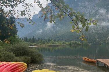 Blick auf einen Bergsee. Im Vordergrund liegen rote und gelbe Kanus.