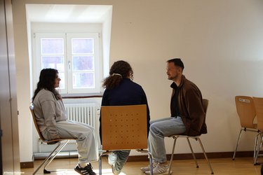 Drei Studierende sitzen sich auf Stühlen gegenüber und unterhalten sich