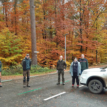 Gruppenfoto der Exkursionsteilnehmer auf einer Straße im Wald. Daneben steht ein geparktes Auto.