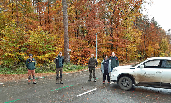 Gruppenfoto der Exkursionsteilnehmer auf einer Straße im Wald. Daneben steht ein geparktes Auto.