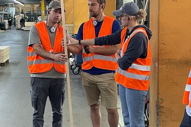 Studierende stehen im Sägewerk und hören dem Referenten zu