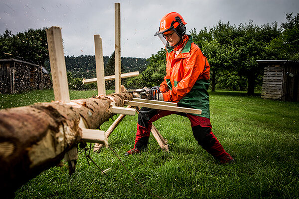 Waldarbeiterin beim Entasten eines Baumstammes mit der Motorsäge an einer Übungseinrichtung