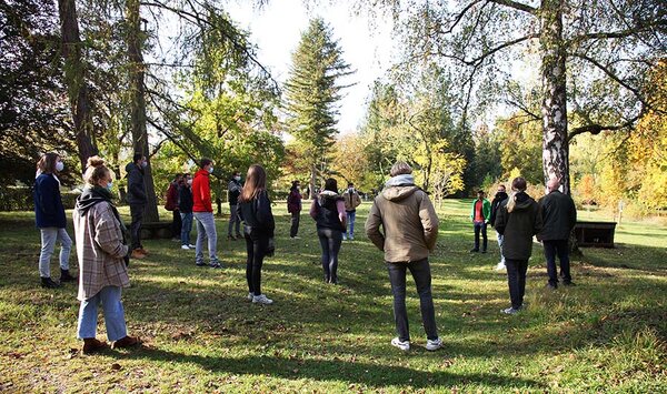Studienanfänger stehen mit Abstand im Arboretum und hören den Studiengangkoordinatoren zu. 