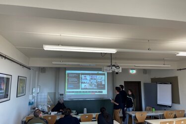 Blick in einen Hörsaal mit der Zoomsitzung auf der Leinwand