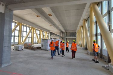 Studiernede stehen mit orangenen Warnwesten und Helmen auf der Baustelle
