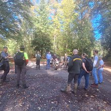 Studierende und Dozenten stehen zusammen auf einem Waldweg und unterhalten sich