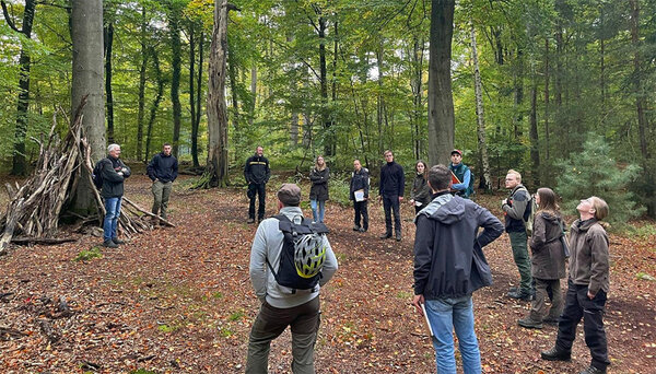 Einge Gruppe Studierende stehen mit dem Förster im Wald. Der Förster erklärt den Studierenden die besonderen Ansprüche an einen urbanen Stadtwald.
