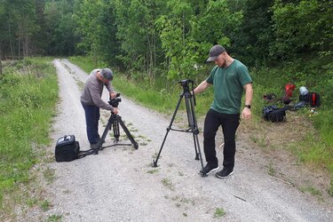 Zwei Kameramänner stellen Ihre Stative auf einem Waldweg auf