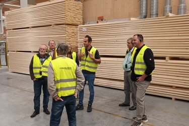 Teilnehmer stehen mit gelben Warnwesten in einem Sägewerk