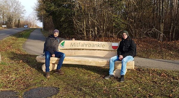 Zwei Studierende sitzen auf dem Mitfahrbänkle