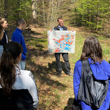 Prof. Bertil Burian steht mit Studierenden im Wald und zeigt eine Karte vom Rammert. Neben grundlegenden Infos zur Geographie sowie den verschiedenen Baumarten, teilt Herr Burian auch vertiefendes forstwirtschaftliches Wissen mit. 