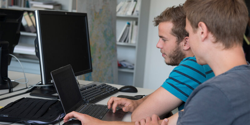Zwei Studenten arbeiten zusammen an einem PC und Notebook im GIS-Labor der Hochschule Rottenburg