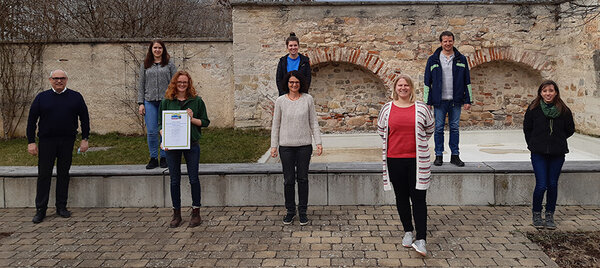 Gruppenfoto mit der Steuerungsgruppe. Mitglieder halten die Auszeichnungsurkunde in die Kamera.