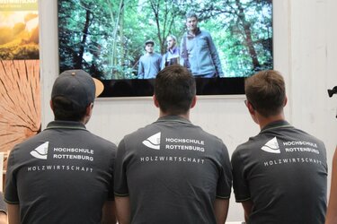 Messebesucher schauen sich auf dem Messestand den Imagefilm der Hochschule Rottenburg an