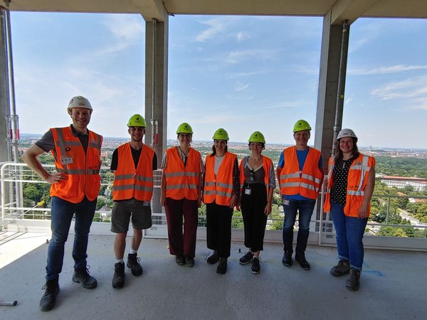 Gruppenfoto der Teilnehmer auf der Bausstelle mit orangenen Warnwesten und Helmen