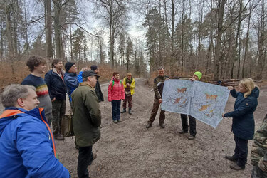 Die Teilnehmer stehen im Wald um die Referenten. Die Referenten halten eine Karte in der Hand.