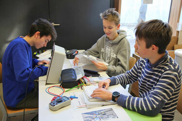 Schüler und Schülerinnen in Kleingruppen an verschiedenen Versuchsstationen zum Thema „Erneuerbare Energien“