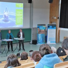 Die Referenten stehen auf der Bühne der Aula.