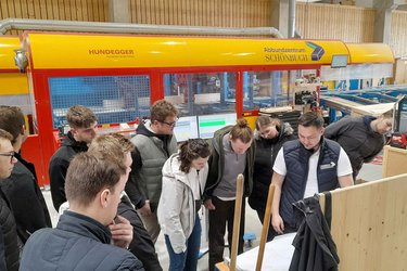 Studierende stehen in der Werkshalle und hören dem Referenten zu