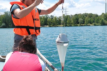 Studierende sitzen und stehen im Boot und nehmen Wasserproben