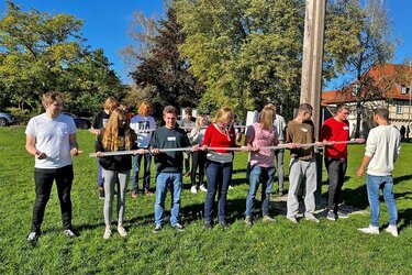 Studienanfänger spielen zusammen ein Geschicklichkeitsspiel auf der Wiese vor den Hochschulgebäuden