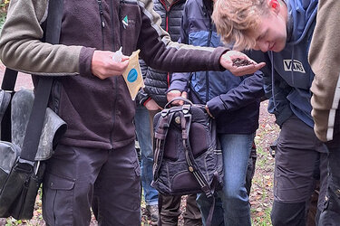Studierende stehen um den Referenten draußen im Wald