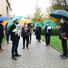 Die Delegation steht vor dem Hochschulgebäude mit aufgespannten Regenschirmen und Mundschutz