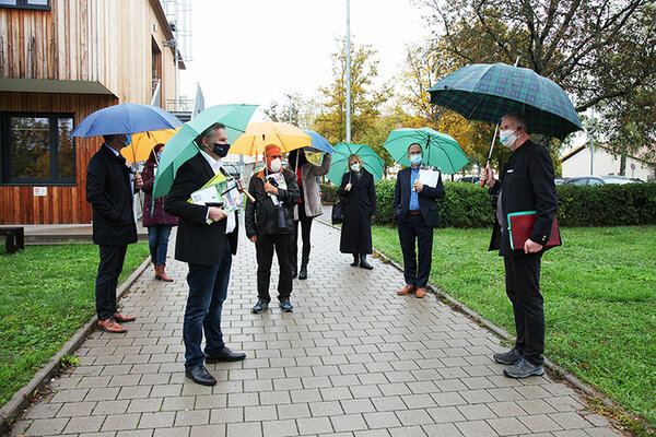 Die Delegation steht vor dem Hochschulgebäude mit aufgespannten Regenschirmen und Mundschutz