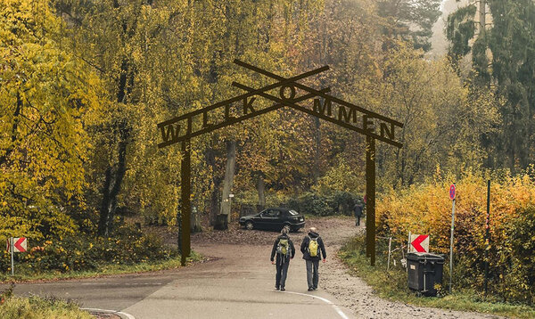 Wanderer durschreiten ein Eingangstor zum Waldparkplatz mit der Beschriftung Willkommen