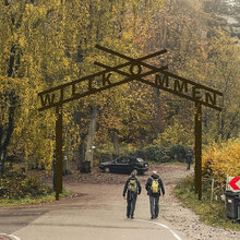 Wanderer durschreiten ein Eingangstor zum Waldparkplatz mit der Beschriftung Willkommen