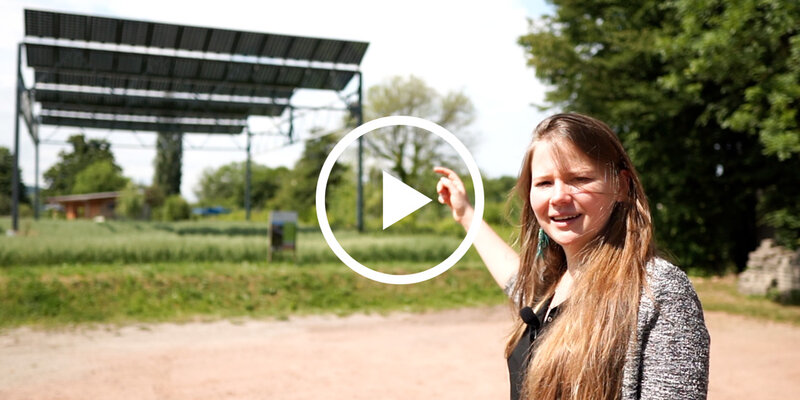 Studierende zeigt auf eine Photovoltaikanlage im Hintergrund