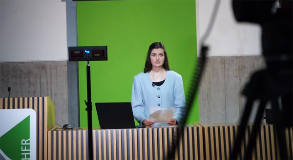 Studierende vor einem Greenscreen in der Aula der Hochschule Rottenburg. Im Vordergrund stehen Leuchten und Kameras.