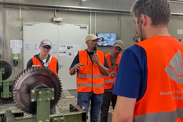 Studierende stehen im Sägewerk und hören dem Referenten zu