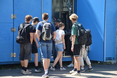 Studierende stehen in einer Gruppe und hören dem Dozenten zu