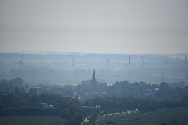 Landschaftsfoto mit Dorf. Im Hintergrund sechs Windräder.