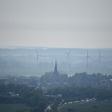 Landschaftsfoto mit Dorf. Im Hintergrund sechs Windräder.