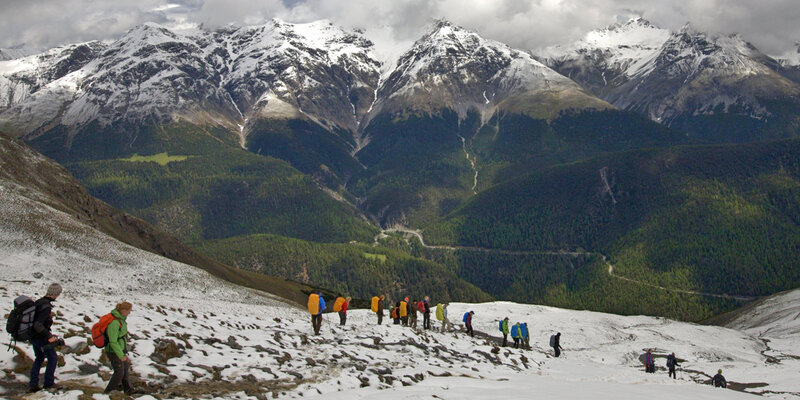 Studierende wandern bei einer Exkursion über ein Schneefeld. Im Hintergrund schneebedeckte Berggipfel. 