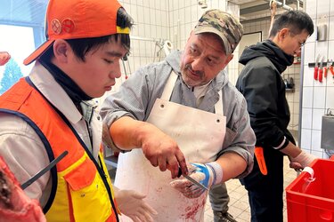 Ein Metzger steht in der Wildkammer und erklärt den Gästen etwas