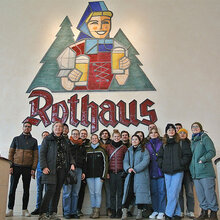 Gruppenfoto mit den Exkursionsteilnehmern in der Brauerei vor dem Logo