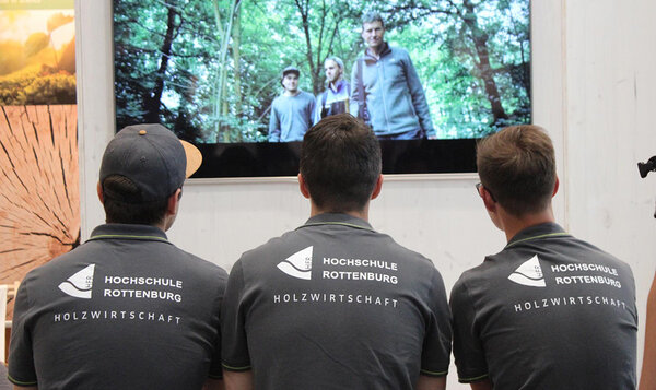 Studierende schauen auf einen Monitor auf dem Messestand, auf dem der Imagefilm der Hochschule zu sehen ist