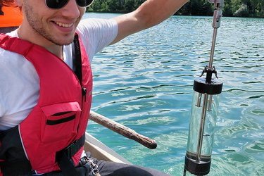Ein Student sitzt im Boot und nimmt eine Wasserprobe