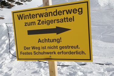 Hinweisschild auf dem Winterwanderweg zum Zeigersattel mit dem Text: Achtung! Der Weg ist nicht gestreut. Festes Schuhwerk erforderlich. 